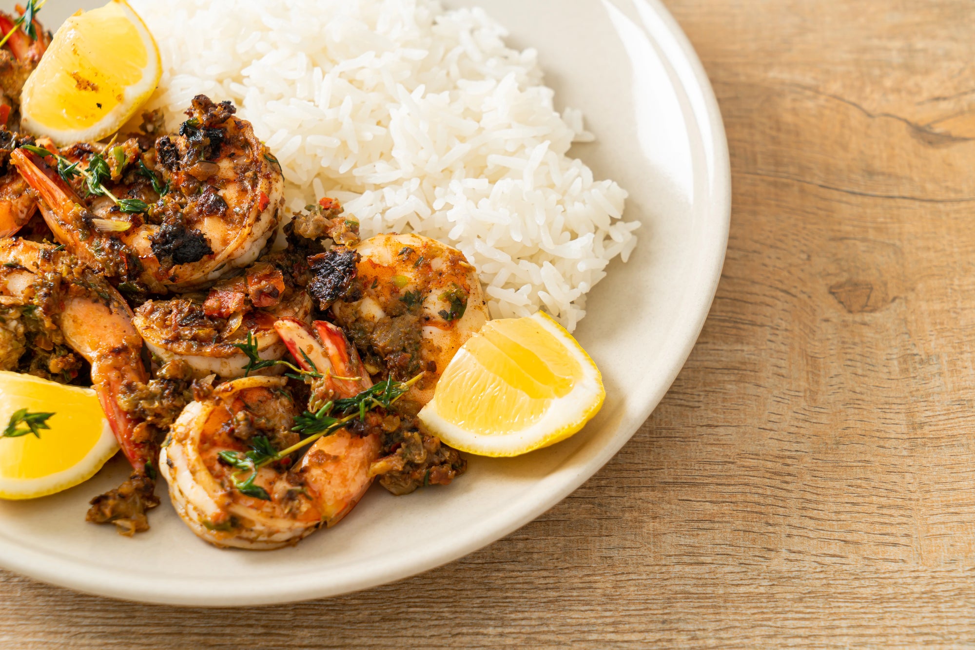 Plated dish of shrimp with lemon wedges and white rice on a wooden table.